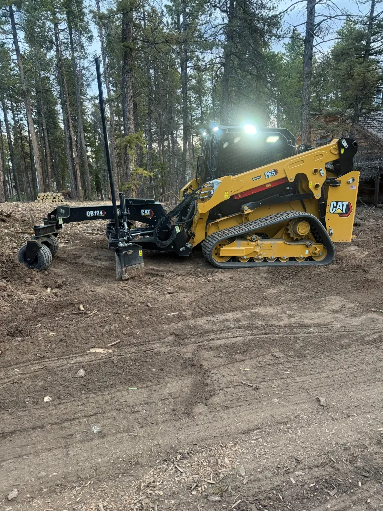 CAT compact track loader cutting a new driveway through Northern Colorado foothill pines, dirt freshly turned with proper crown for runoff.