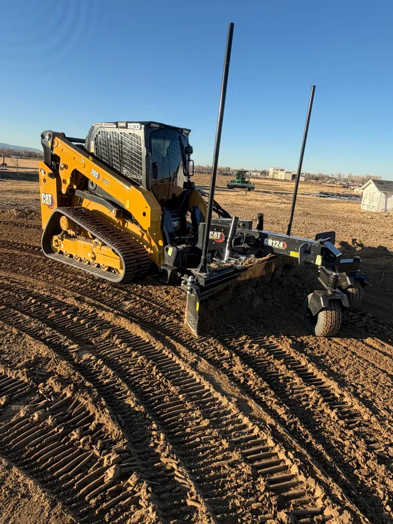 Caterpillar compact track loader with grading attachment laying down a survey-grade finish on a residential lot in Windsor, Colorado.